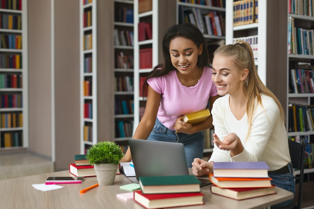 Afro girl helping blonde classmate with educational program